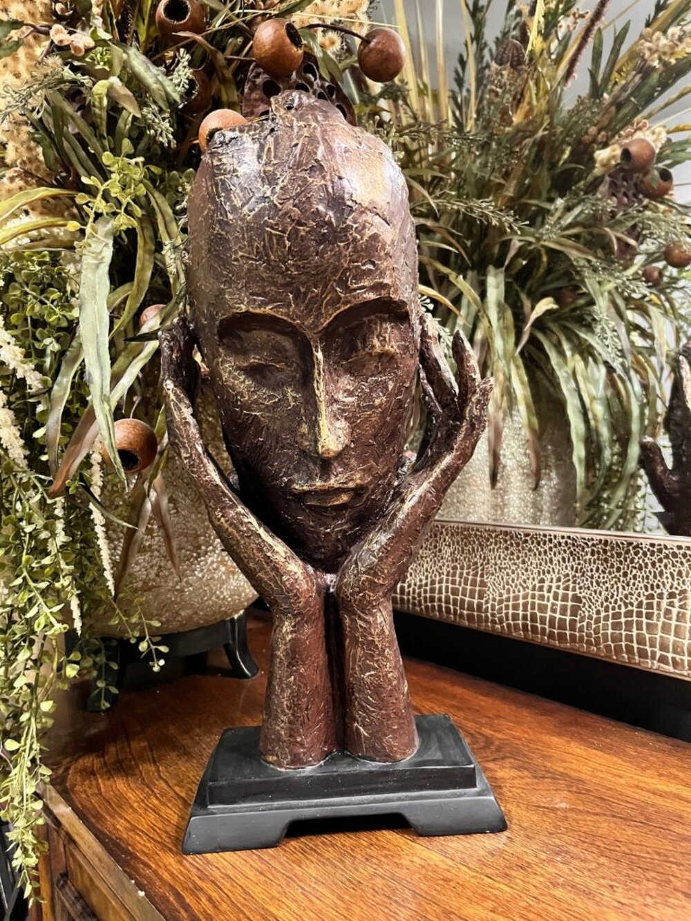 bronze-toned sculpture depicting contemplative face resting on hands